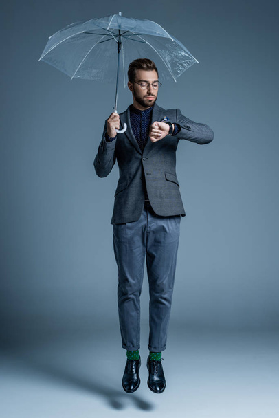Man with umbrella looking at watch - Φωτογραφία, εικόνα