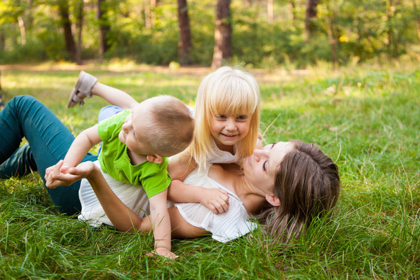 Mother and her daughter and son together playing and laughing on the grass - Photo, Image
