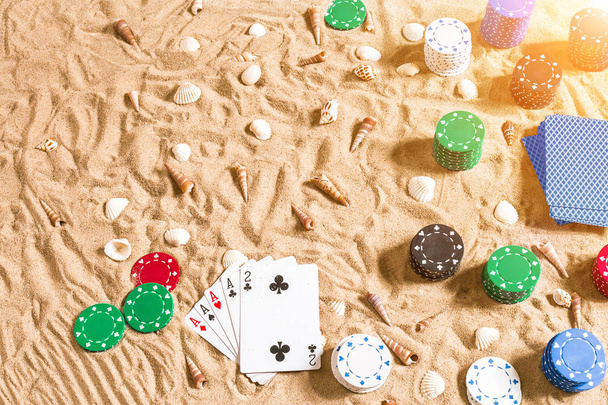 Szerencsejáték a pihenés fogalmát - fehér homok, tengeri kagylókból, színes zsetonok és kártyák. Szemközti nézet - Fotó, kép