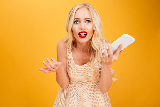 Confused shocked young blonde woman using mobile phone. - Photo, image