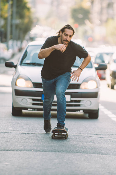 Pro skateboard rider in front of car on city street - Фото, изображение