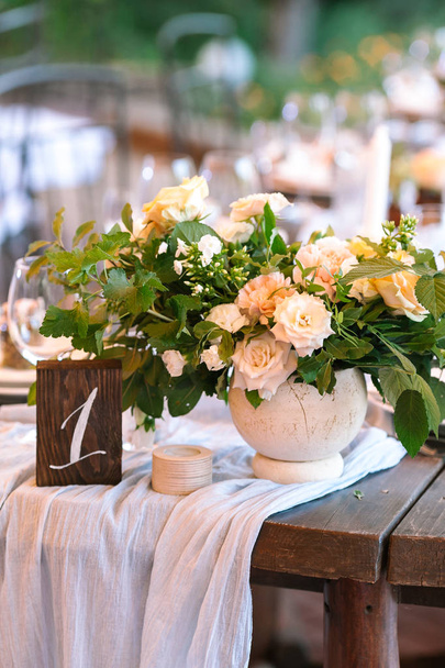 flora, wedding concept. delicate yellow and creamy roses mixed in bouquet for wedding decoration and placed among such verdure as leaves of oak, rosebush and raspberry in the vase of table number one - Photo, Image