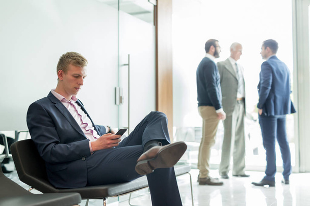 Biznesmen korzystający ze smartfona podczas siedzenia w poczekalni. - Zdjęcie, obraz