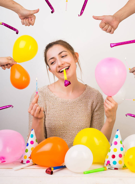 holidays, weekends, beauty concept. wonderful girl with charming smile with birthday whistle in her teeth, she is holding small pinl balloon and blue candle for cake - Foto, Imagem