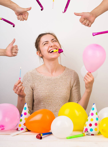 party, celebration, birthday concept. extremelly happy young girl is shrieking with laughter, holding small pink balloon in one arm, blue candle in other and birthday whistle with her teeth - 写真・画像