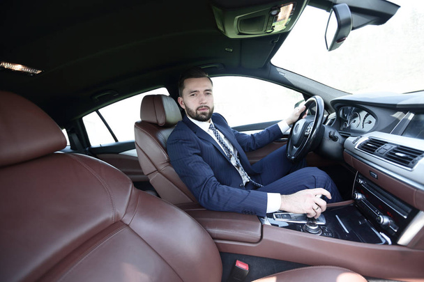 View from the side confident businessman sits at the wheel of a car - 写真・画像