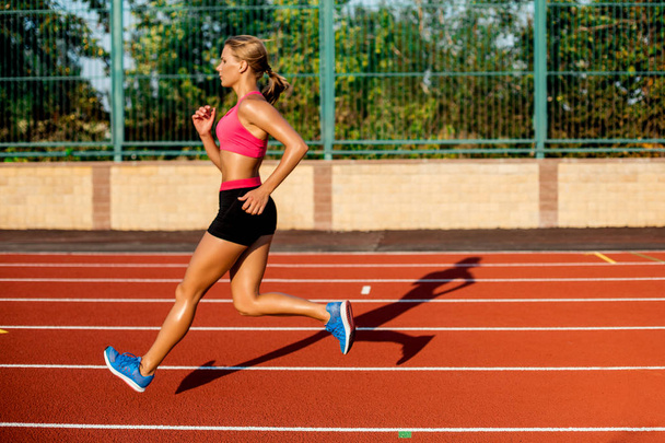 Vista lateral hermosa mujer joven ejercicio correr y correr en pista atlética en el estadio
 - Foto, Imagen