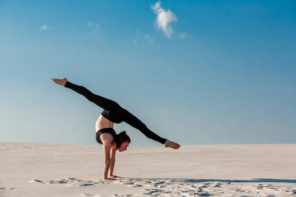 Young woman practicing handstand on beach with white sand and bright blue sky - Photo, Image