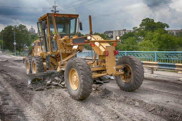 nivelador amarillo que conduce en el camino del asfalto en el verano
 - Foto, imagen
