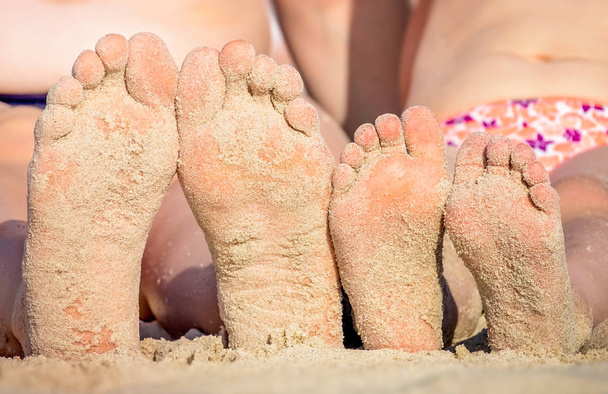 Мати і дочка ноги вкриті пляжним піском
 - Фото, зображення
