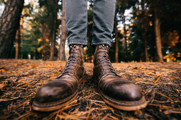 Pernas de homem em botas de couro vintage cortador de madeira e jeans cortados de pé na floresta de outono no chão. Cores de queda e conceito de humor. Sapatos confortáveis. Caminhando no fim de semana na natureza. Distorção da lente.  - Foto, Imagem