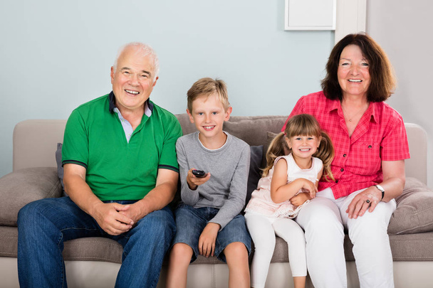 Boldog nagyszülők, unokák ül a díványon, a nappaliban nézi a televíziót - Fotó, kép