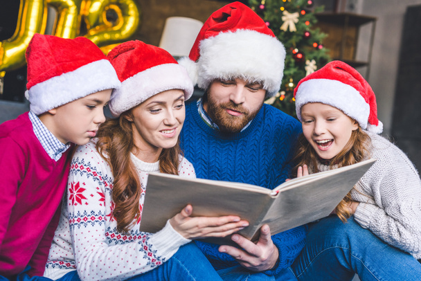 Familie mit Weihnachtsmannhüten liest Buch - Foto, Bild