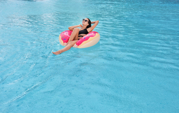Beautiful young woman on inflatable donut in swimming pool - Fotoğraf, Görsel