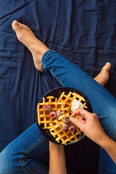 Belgian waffles with cream and frozen raspberries on blue ceramic plate in woman' s hands. Top view - Fotografie, Obrázek