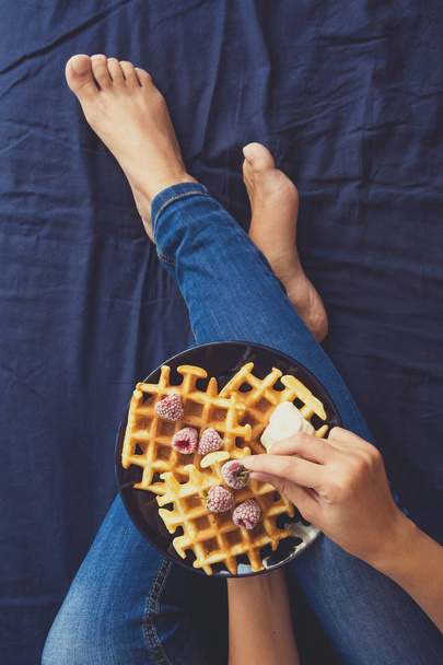 Belgian waffles with cream and frozen raspberries on blue ceramic plate in woman' s hands. Top view - Foto, Imagen