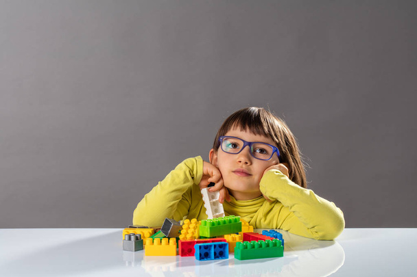 thoughtful young girl with serious eyeglasses playing with building blocks - 写真・画像