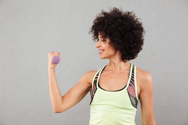 Sonriente mujer de fitness haciendo ejercicio con mancuerna en el estudio
 - Foto, Imagen