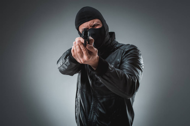 Грабитель или террорист в черной маске, стреляющий из пистолета
. - Фото, изображение