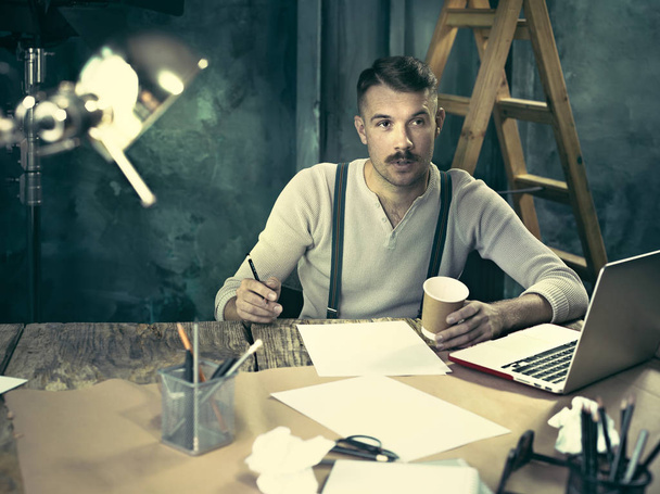Portrait of a bearded businessman who is working with his notebook at loft studio. - Фото, зображення