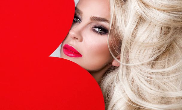 Beautiful woman with long blond hair standing on a white background dressed in red underwear and holds in his hands a red heart Valentine's Day - Fotoğraf, Görsel