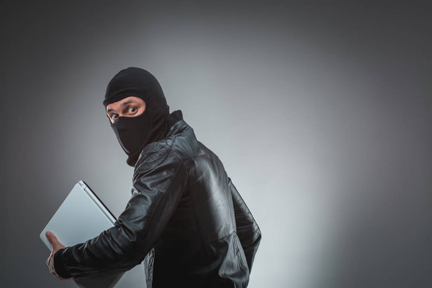 Ladrón robando una computadora portátil. Aislado sobre fondo gris
 - Foto, imagen