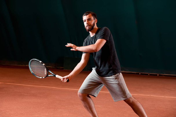 Guapo joven en camiseta sosteniendo raqueta de tenis en pista de tenis
 - Foto, imagen