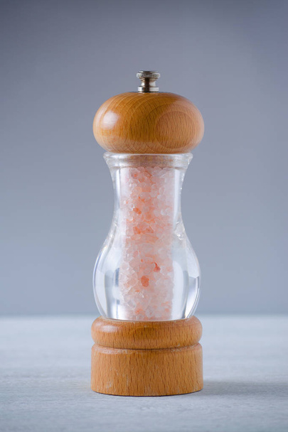 cristais de sal rosa himalaia em um moedor de madeira de vidro em cinza
 - Foto, Imagem