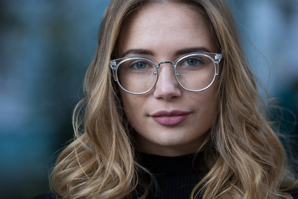 Myopia, close-up portrait of young woman student in eyeglasses for good vision look at camera, blue building background - Foto, Bild