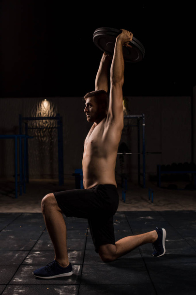 Νέοι μυϊκής εκγύμνασης αρσενικό μοντέλο κάνει αλτήρα ασκήσεις lunge στο πάρκο. - Φωτογραφία, εικόνα