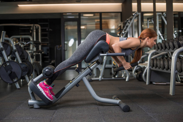 Muskulöse junge Frau macht im Fitnessstudio Übungen auf dem Simulator - Foto, Bild