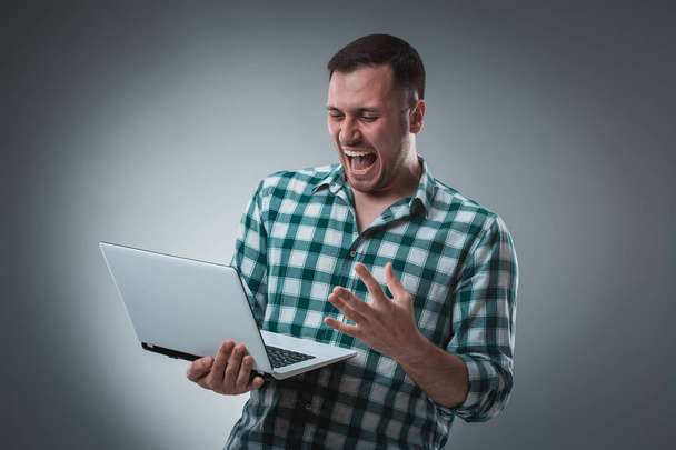 Atraktivní obchodní model muž v zelené tričko izolované na šedé pracují s notebookem, ukazující něco levou rukou. - Fotografie, Obrázek