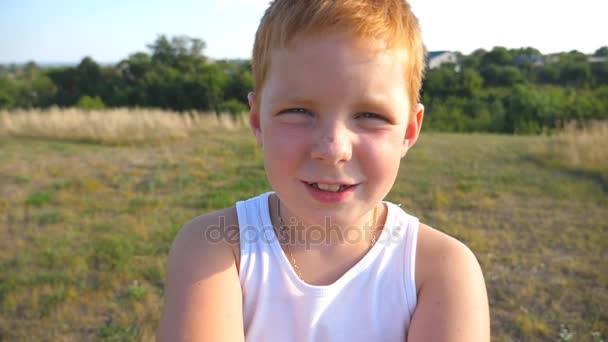 Érzelmek az arcán boldog kifejezés gyermek közelről. Boldog vörös hajú fiú szeplő szabadtéri portréja. Imádnivaló szép baba látszó-ba kamera örömteli mosollyal. Lassú mozgás - Felvétel, videó
