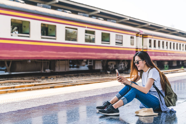 Asian tourist teenage girl at train station using smartphone map, social media check-in, or buy ticket booking. Modern travel app technology, lone traveler, Summer vacation railroad adventure concept - Foto, immagini