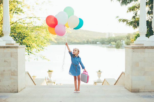 Vrolijk meisje houdt van kleurrijke ballonnen en kinderachtig koffer - Foto, afbeelding