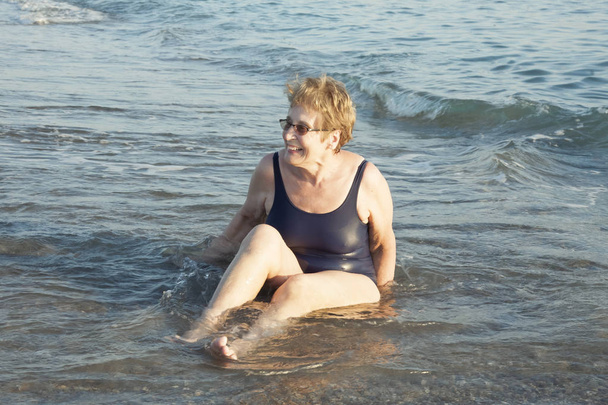 Portrét krásné starší ženy sedící na písku a užívající si mořských vln. Koncept dovolené a cestování. - Fotografie, Obrázek