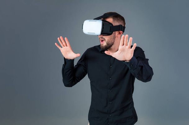 Joven emocional usando un auricular VR y experimentando la realidad virtual sobre fondo gris
 - Foto, imagen