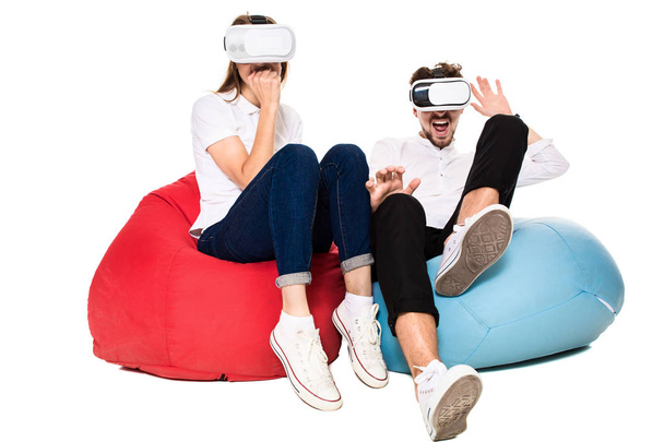 Excited young couple experiencing virtual reality seated on beanbags isolated on white background - Foto, immagini