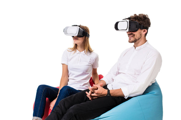 Excited young couple experiencing virtual reality seated on beanbags isolated on white background - Фото, зображення