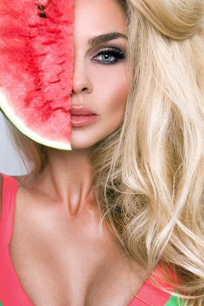 Beautiful female model with long blond hair, holding a watermelon at her face - Photo, Image