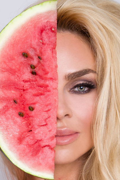Beautiful female model with long blond hair, holding a watermelon at her face - Photo, Image