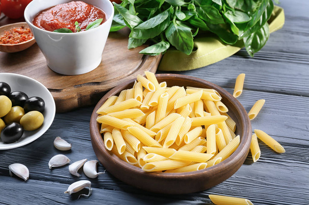Kom met pasta en olijven op houten tafel - Foto, afbeelding