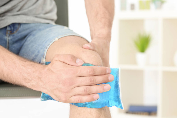 Young man applying cold compress to leg at home - Photo, image