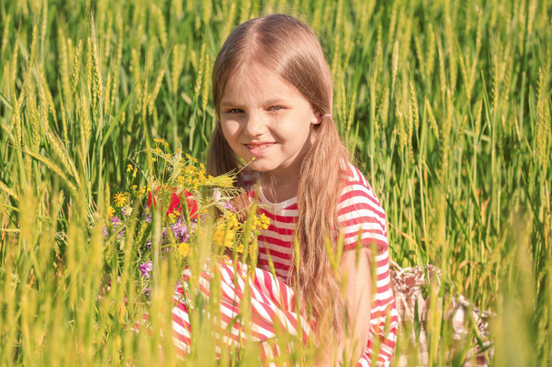 Little girl with bouquet of wildflowers in green field - Фото, зображення
