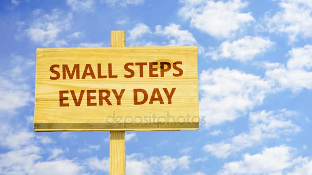 Small steps every day. Words on a wooden sign against time lapse clouds in the blue sky. - Footage, Video