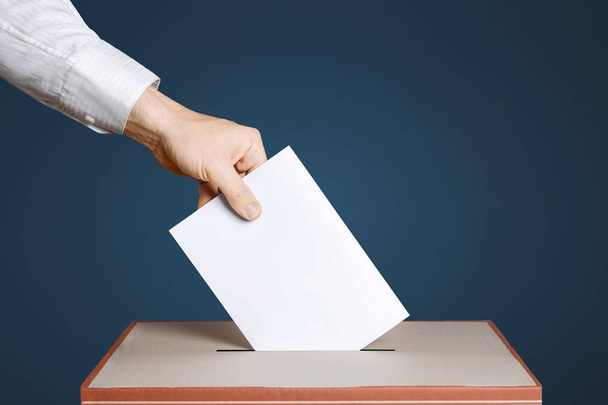 Voter Holds Envelope In Hand Above Vote Ballot. Blue background. Democracy Concept - Foto, Imagen