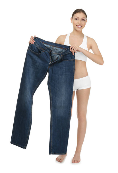 Beautiful young woman with oversized jeans on white background. Diet concept - Photo, Image