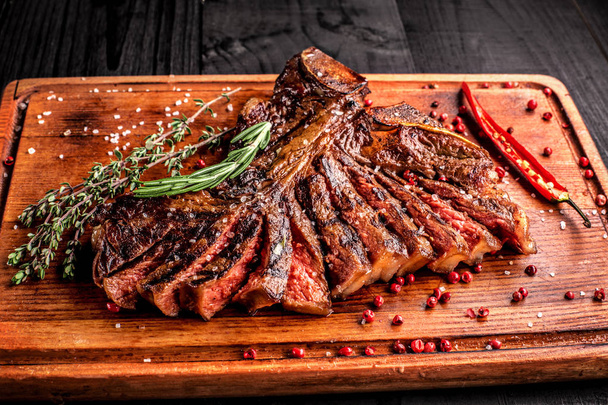 Sliced medium rare grilled steak on rustic cutting board with rosemary and spices , dark rustic wooden background, top view - Photo, Image
