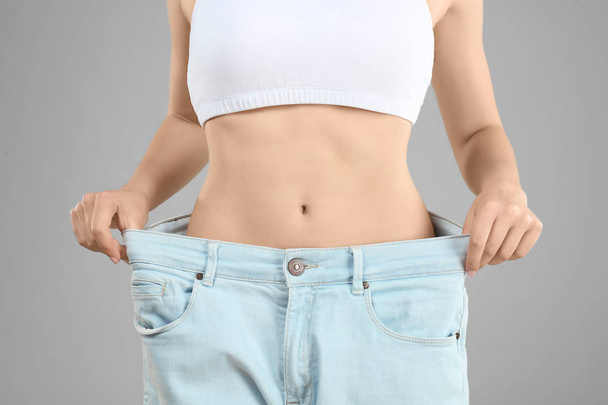 Young woman in oversized jeans on gray background, closeup. Diet concept - Fotó, kép
