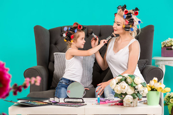 Mom and daughter in the studio on the sofa in the curlers make up and have fun - Photo, Image